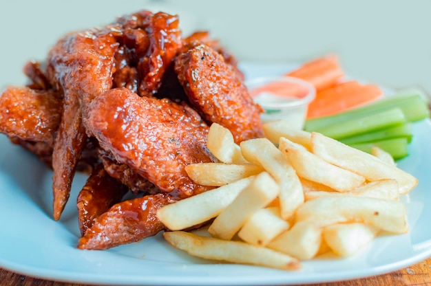 Plate of barbecue wings and fries with ranch sauce Close up of plate of hot wings and fries served on the table National typical food concept