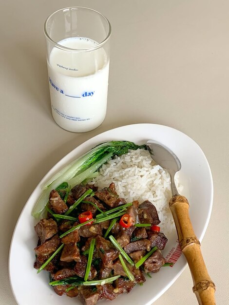 A plate of beef and rice with a glass of milk next to it.