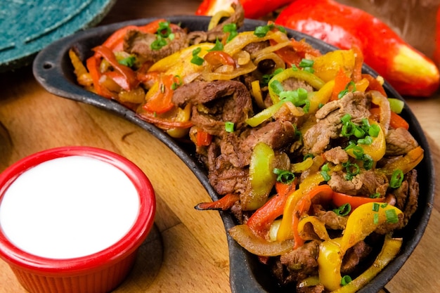 A plate of beef and vegetables with a side of sour cream.