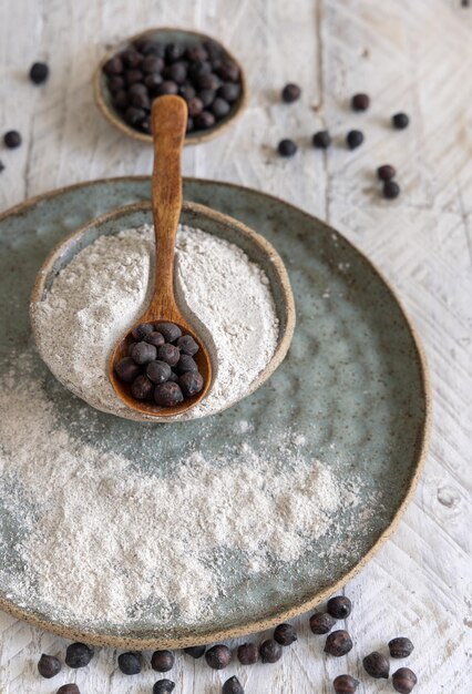 Plate of black chickpea flour and wooden spoon of beans closeup on white wooden table. Traditional beans from Apulia and Basilicata in Italy