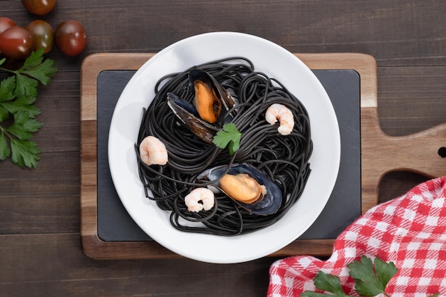 Plate of black pasta with seafood on wooden background. Top view.