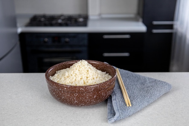 A plate of brown color with golden rice on the table against the backdrop of a dark kitchen Chopsticks lie next to the towel Asian food concept