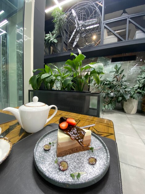 A plate of cake with chocolate on it and a white teapot on the table.