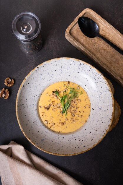 A plate of cheese cream soup with nuts and greens on a dark background top view