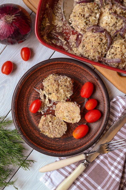 A plate of chicken patties with tomatoes and onions on a table next to a dish of red onions.