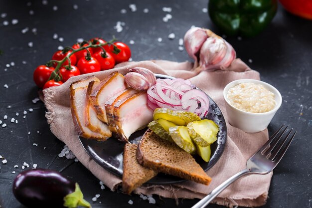 Foto su un piatto antipasto freddo per alcool, fette di pancetta fresca, patate lesse, anelli di cipolla e br nero