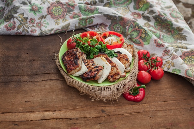 Тарелка вареного мяса, сыра и красных овощей на деревянном столе. Рядом текстильная скатерть с винтажным орнаментом