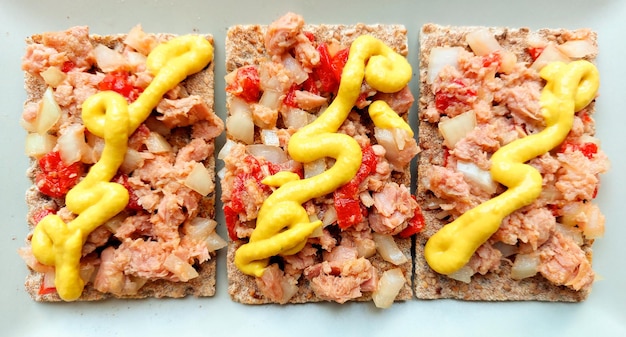 A plate of crackers with different toppings including mustard, red mustard, and mustard.