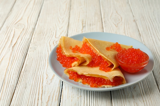 Plate of crepes with red caviar on white wooden surface