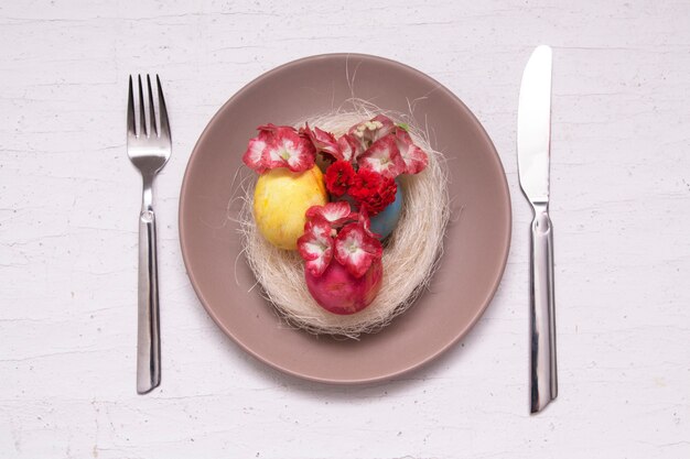 Plate and cutlery with colored eggs, nest and flowers