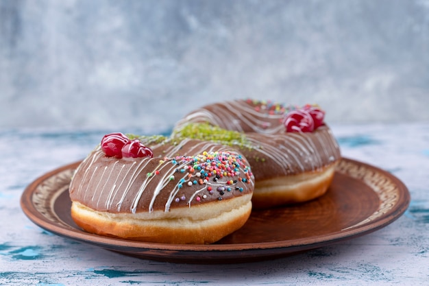 Plate of delicious chocolate donuts with cherry and colorful sprinkles . 