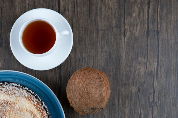 A plate of delicious pie with fresh whole coconut placed on a wooden table .