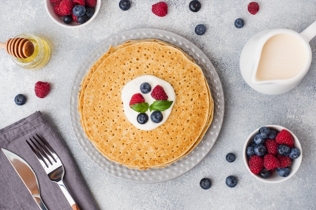 Plate of delicious thin pancakes with berries on grey table 