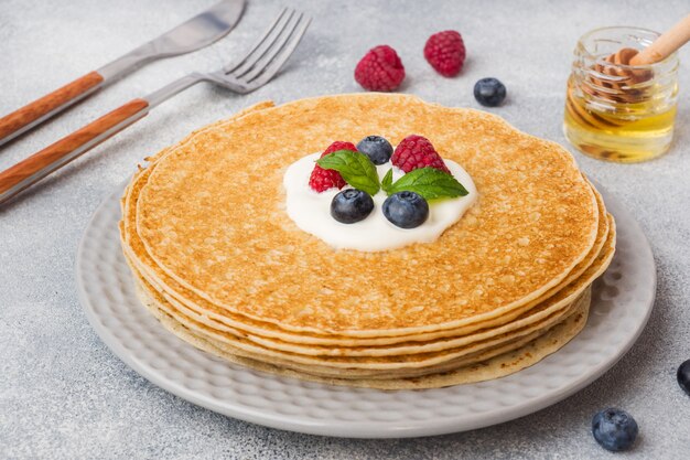 Plate of delicious thin pancakes with berries on grey table 