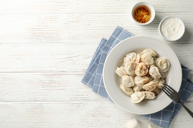 Plate of dumplings with spices on white wooden background, space for text
