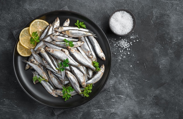 A plate filled with sardines with lemon and parsley on a dark background. Top view, copy space.