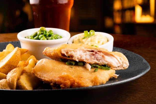 Plate of fish and chips with sliced fried fish and pub table closeup blurred in the background