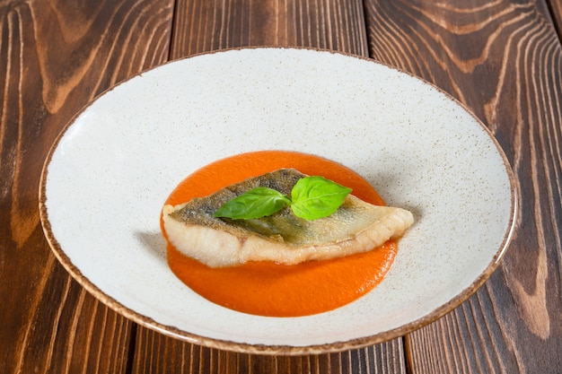 Plate of fish fillet with pumpkin sauce on a wooden table