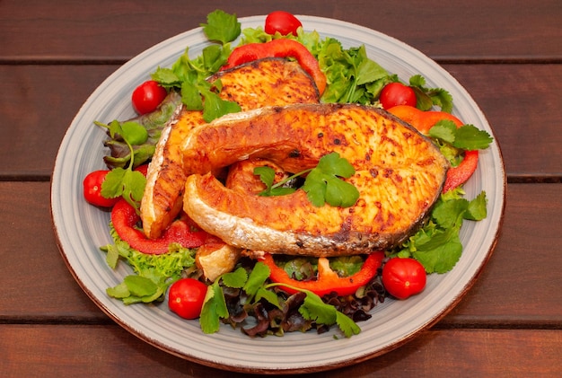 A plate of fish and salad with tomatoes and greens on a wooden table.