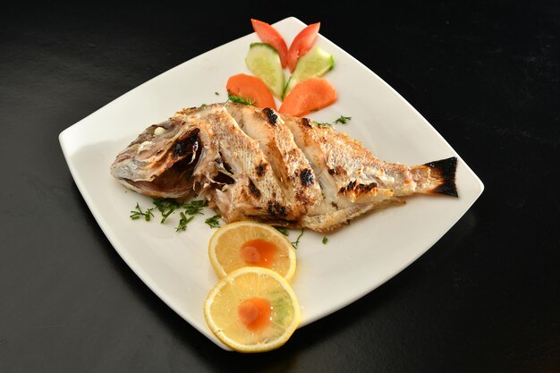 A plate of fish with a lemon and cucumber slices on it