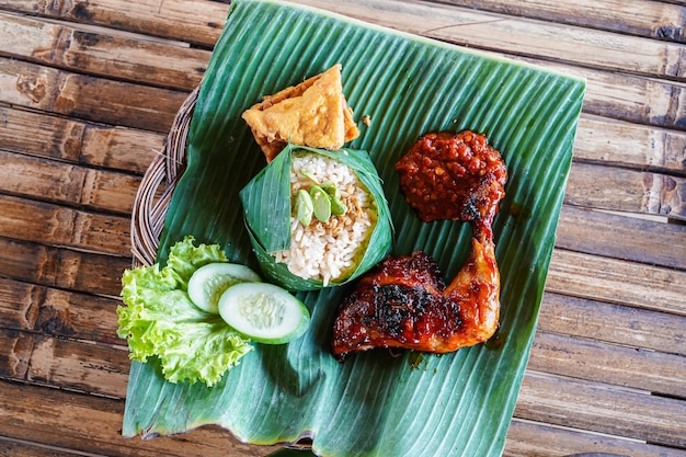 A plate of food with a banana leaf and a chicken leg.