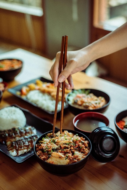 Photo a plate of food with chopsticks and a plate of food with a person holding a chopsticks.