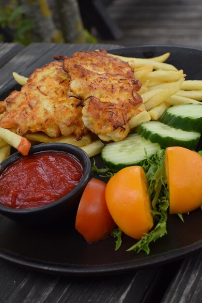 A plate of food with a side of fries and a small container of tomato sauce.