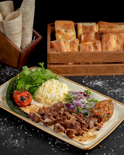 A plate of food with a tray of bread in the background.