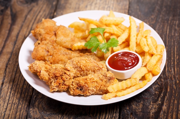 Plate of fried chicken with french fries on a wooden table