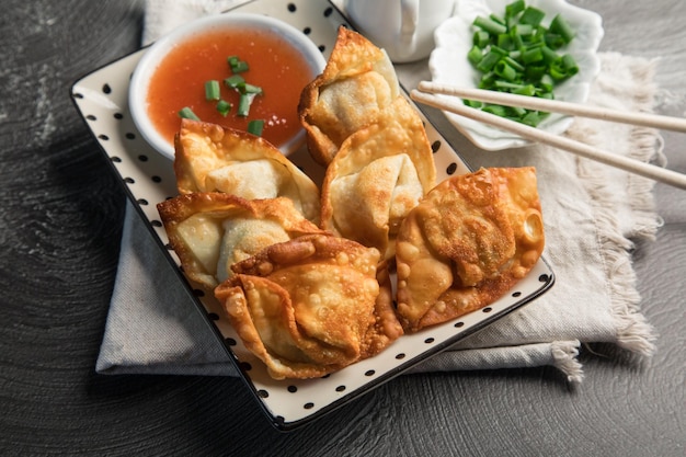 A plate of fried dumplings with a bowl of sauce and green onions on the side