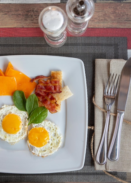 Plate of fried eggs with bacon and vegetables on dark background, top view