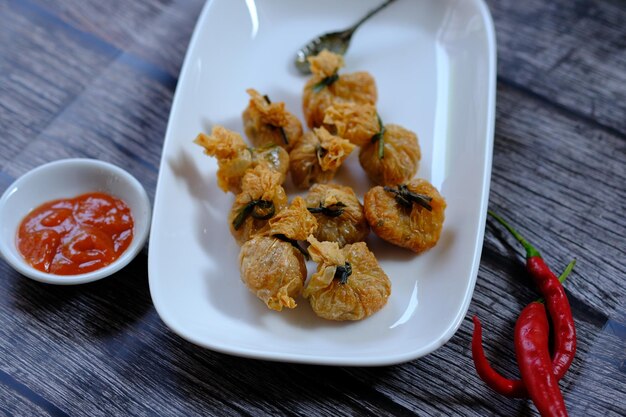 A plate of fried fish with a red chili sauce siomay goreng pangsit goreng