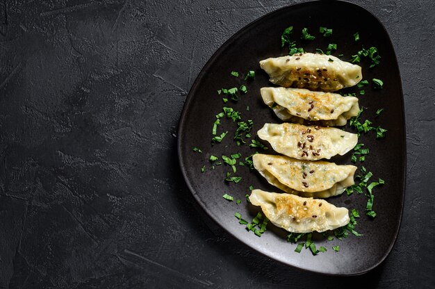 Plate of fried Japanese gyoza dumplings on rustic black table. 