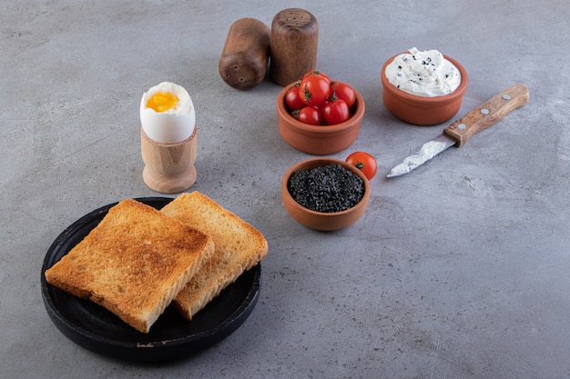 Plate of fried toast, sour cream and boiled egg on stone table.