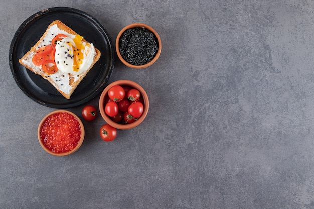 Plate of fried toasts and various caviars on stone table.