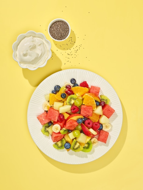 Plate of fruit salad on yellow background, top view