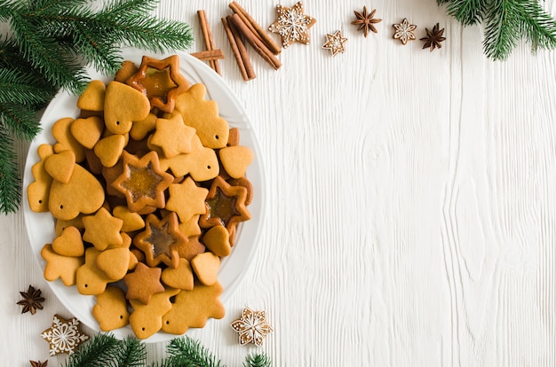 Plate full of freshly baked Christmas gingerbread ready to decorate with icing on white wooden background. Copy space