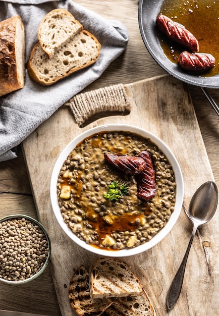 A plate full of lentil legume soup with baked sausage and fresh bread