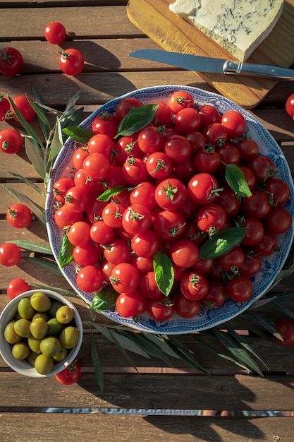 Plate full of ripe cherry tomatoes on a wooden table in sunlight