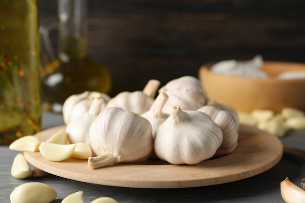 Plate of garlic bulbs, slices, oil on grey table against wooden