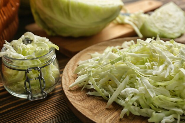 Plate and glass jar with cut cabbage on wooden table, closeup