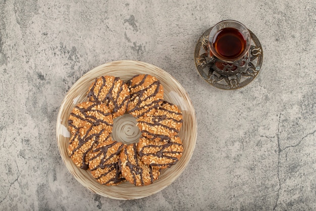 Plate of glazed chip cookies and glass of tea on stone.