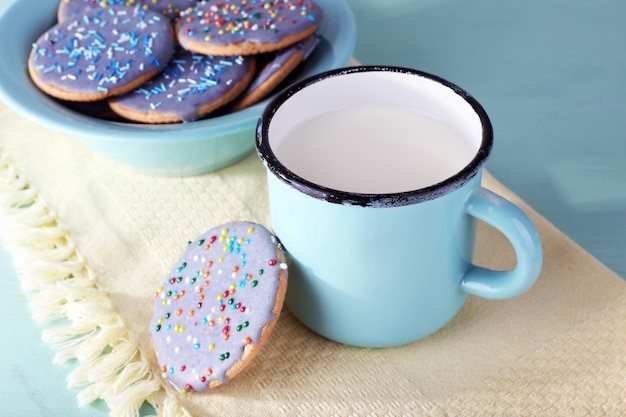 Plate of glazed cookies and mug of milk on napkin and color wooden table background