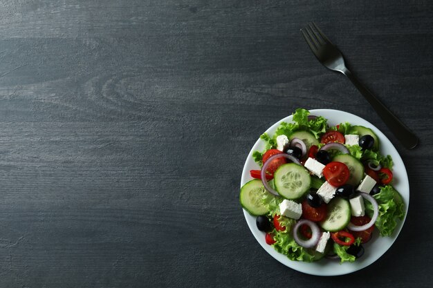 Plate of greek salad and fork on dark wooden background