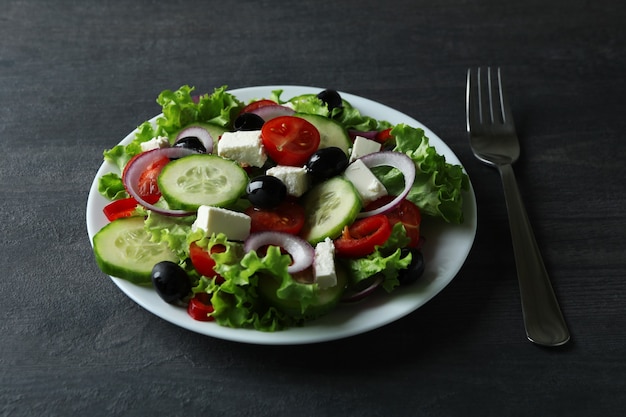 Plate of greek salad and fork on dark wooden background