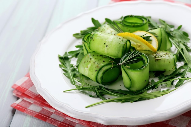 Plate of green salad with cucumber arugula and rosemary on wooden table closeup