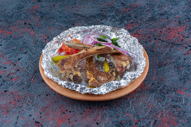 Plate of grilled lamb ribs placed on marble table.