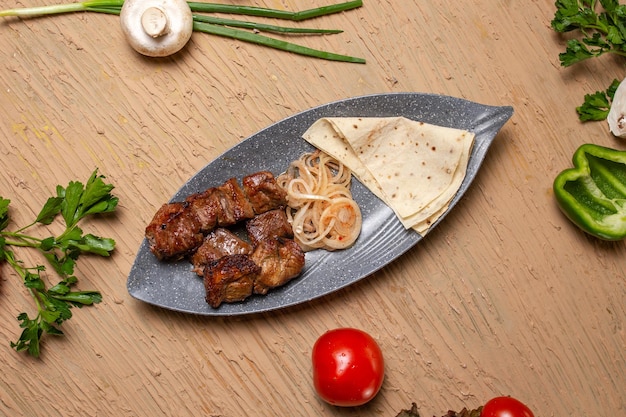 A plate of grilled meat with vegetables and a flatbread on a wooden table