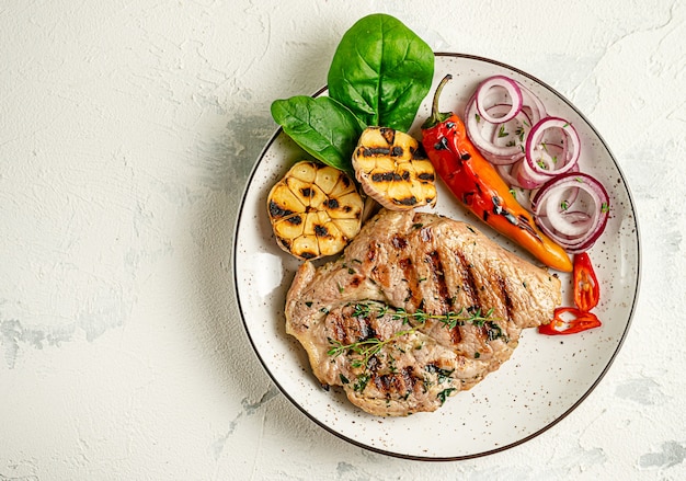 Plate of grilled pork steak with vegetables on concrete background