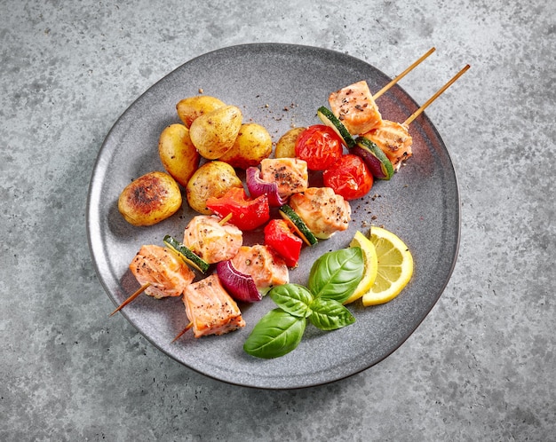 Plate of grilled salmon skewers and vegetables on grey table top view